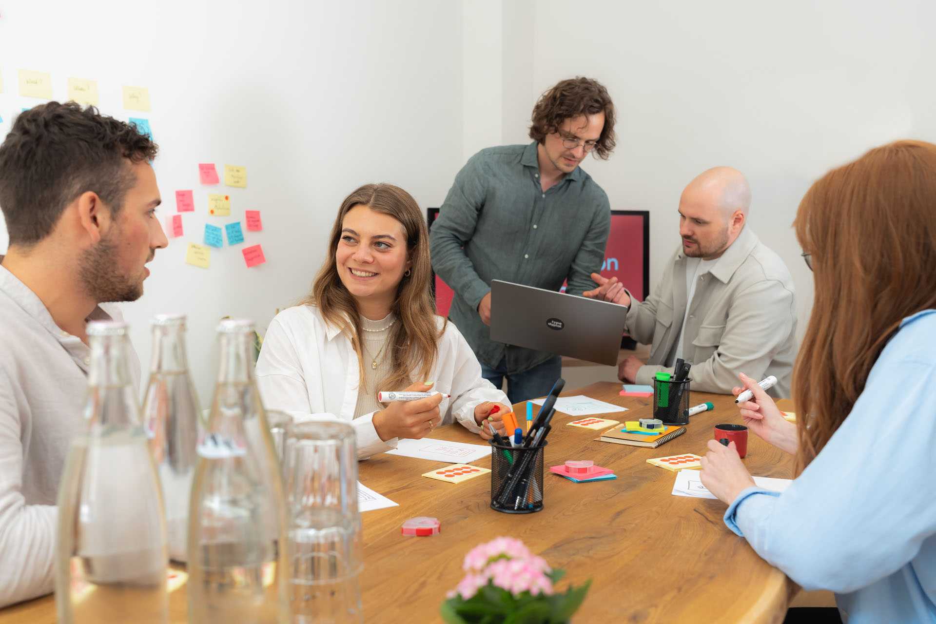 Fünf Personen sitzen am Tisch und befinden sich in einem Workshop. Sie unterhalten sich und machen Notizen.