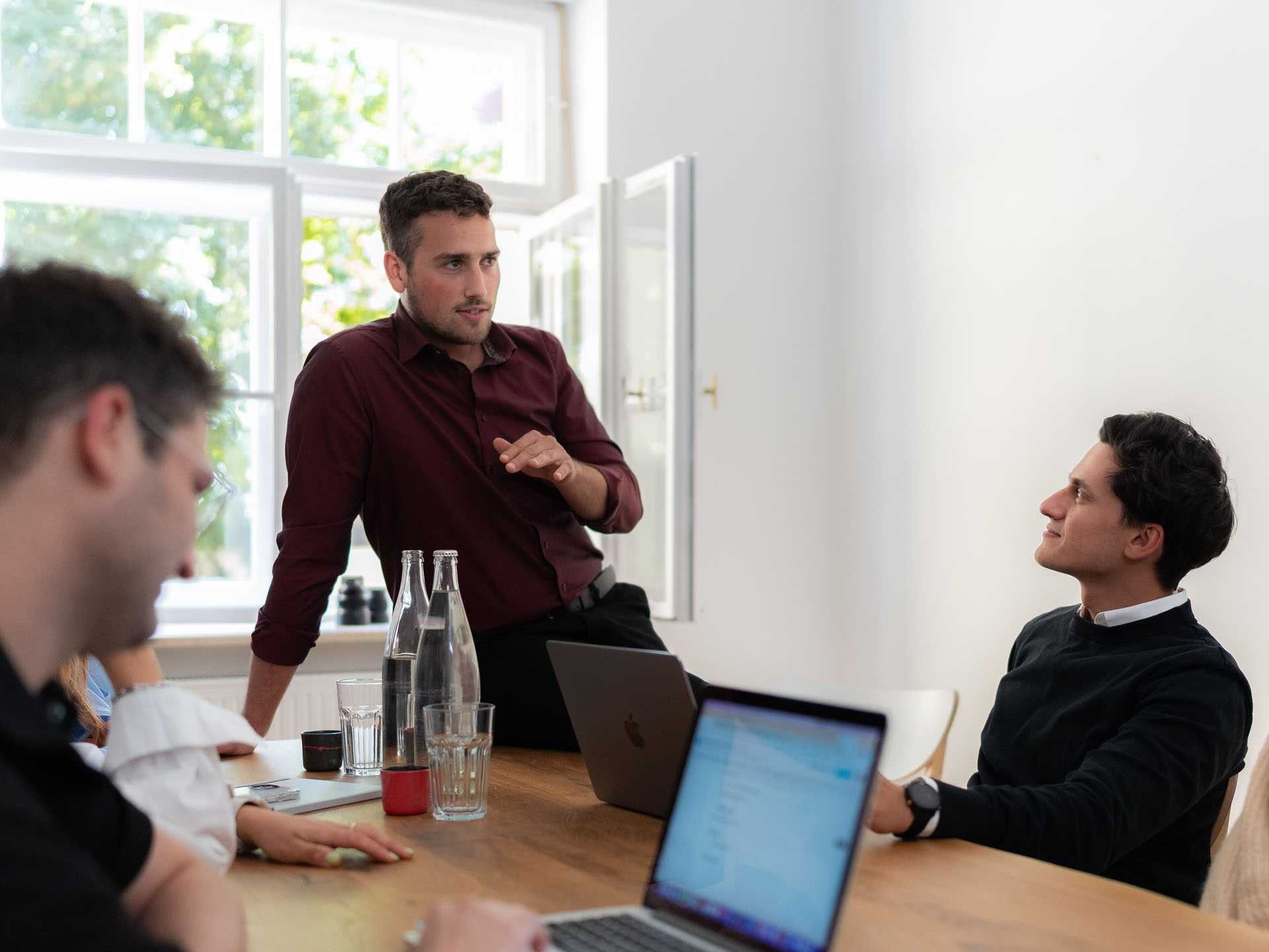 Team sitzt bei entspannter Arbeitsatmosphäre im Meetingraum und Programmierer Falko erklärt etwas.