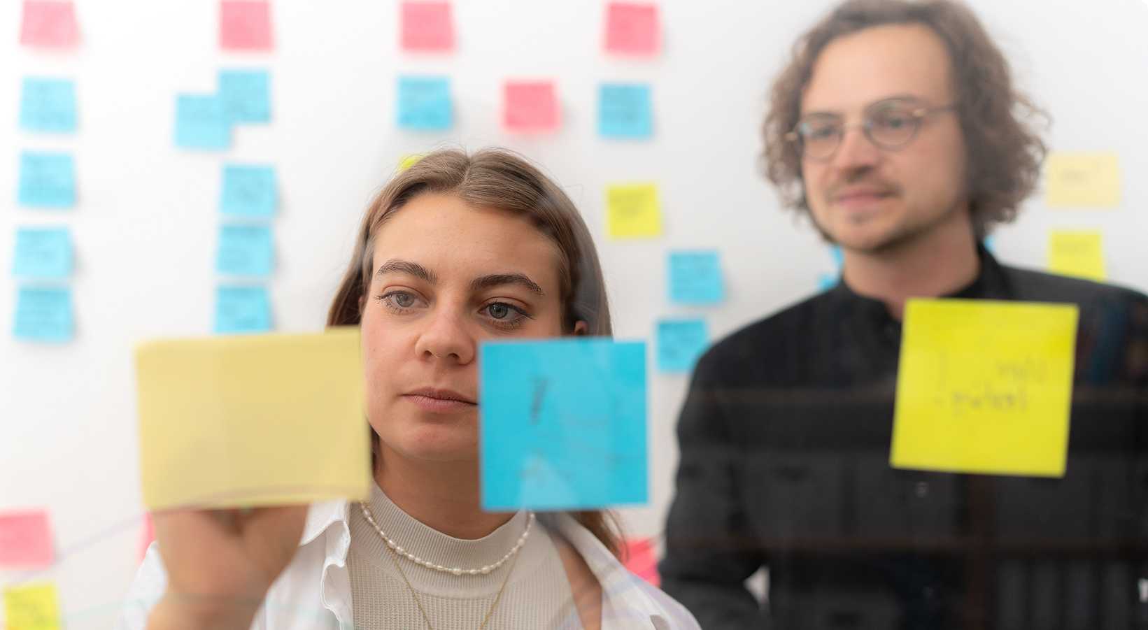 Zwei Personen, die etwas auf ein Sticky-Note schreiben.