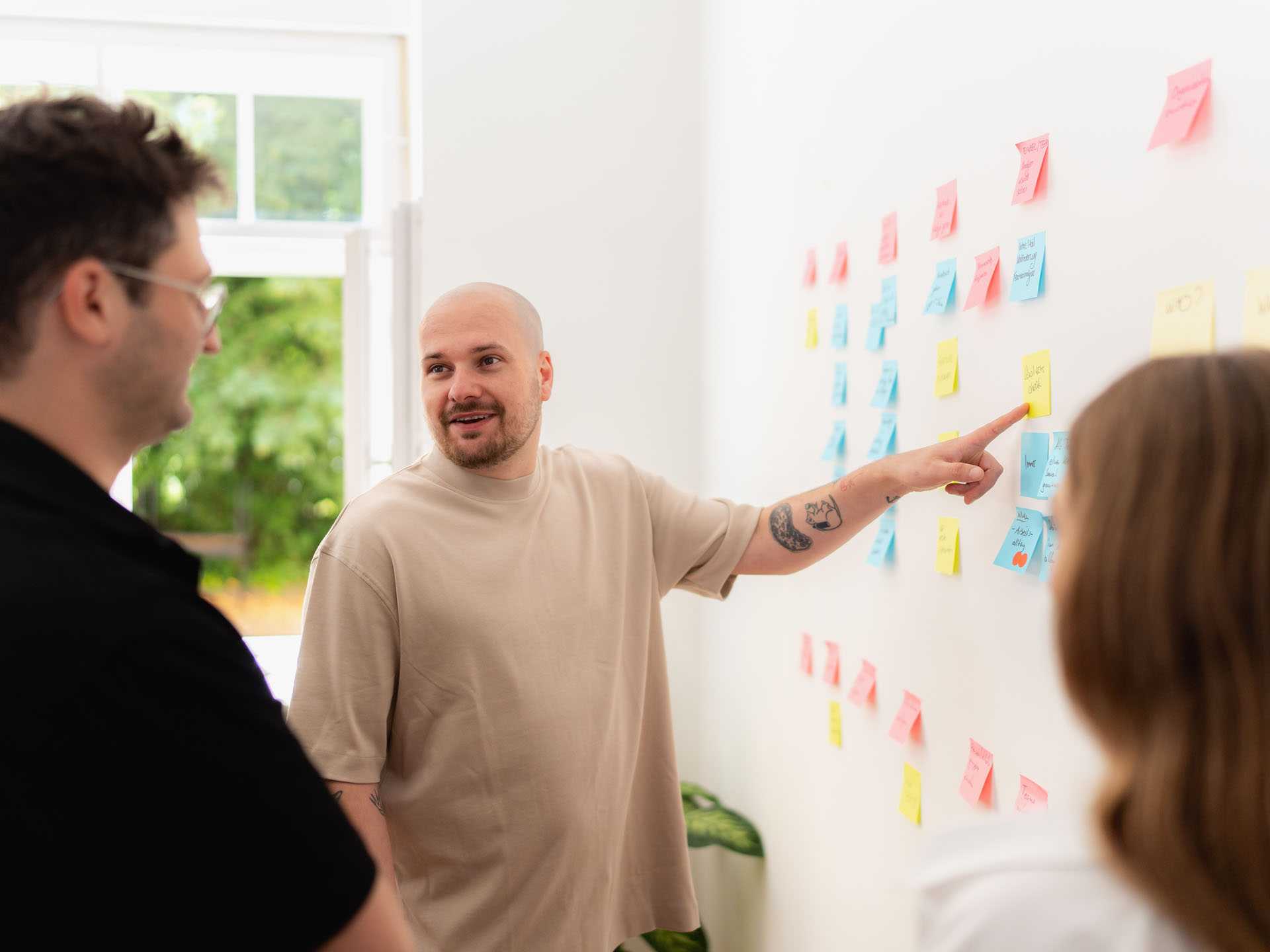 Softwareentwickler AK zeigt etwas auf dem Whiteboard. Er schaut Kalle an.